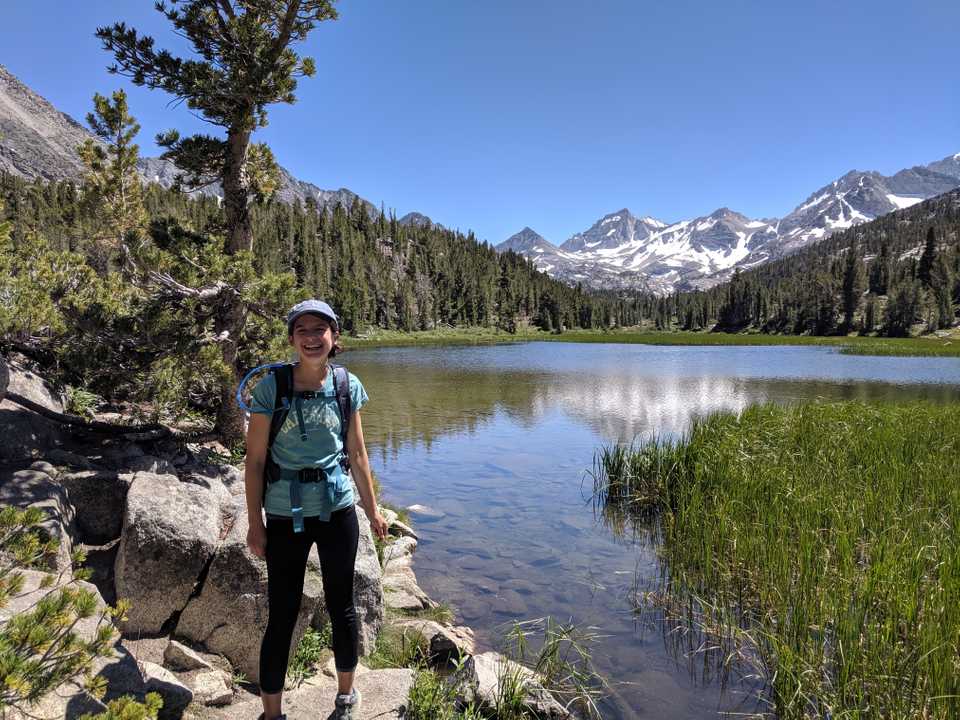 Rebecca hiking in front of a lake in front of snow covered mountains